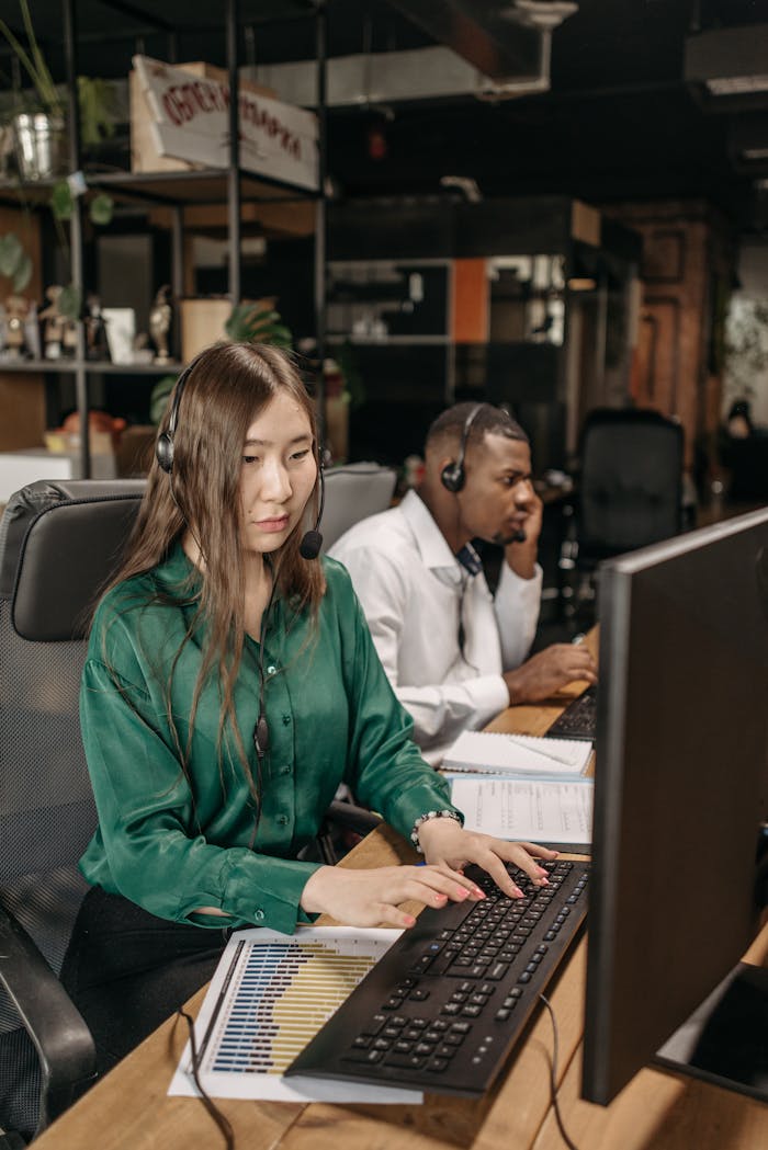 Two diverse employees working in a modern office setting with computers and headsets.